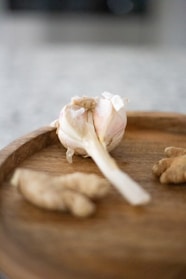 Fresh garlic bulbs and a small bowl of finely ground garlic powder on a wooden board.