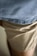 A close-up view of a pair of light beige trousers with a slightly wrinkled texture, partially covered by the bottom edge of a light blue knit fabric.