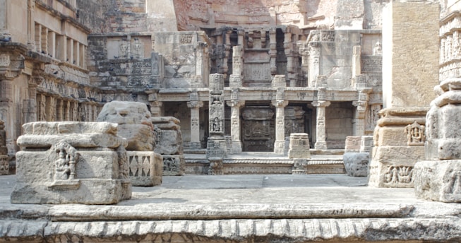 An intricately carved stone structure featuring numerous columns and detailed relief work on the walls. The architecture suggests an ancient or historical site with weathered stones and a mix of angular and rounded shapes. The scene appears to be part of a larger complex, showcasing classical architecture elements with artistic designs etched into the stone.