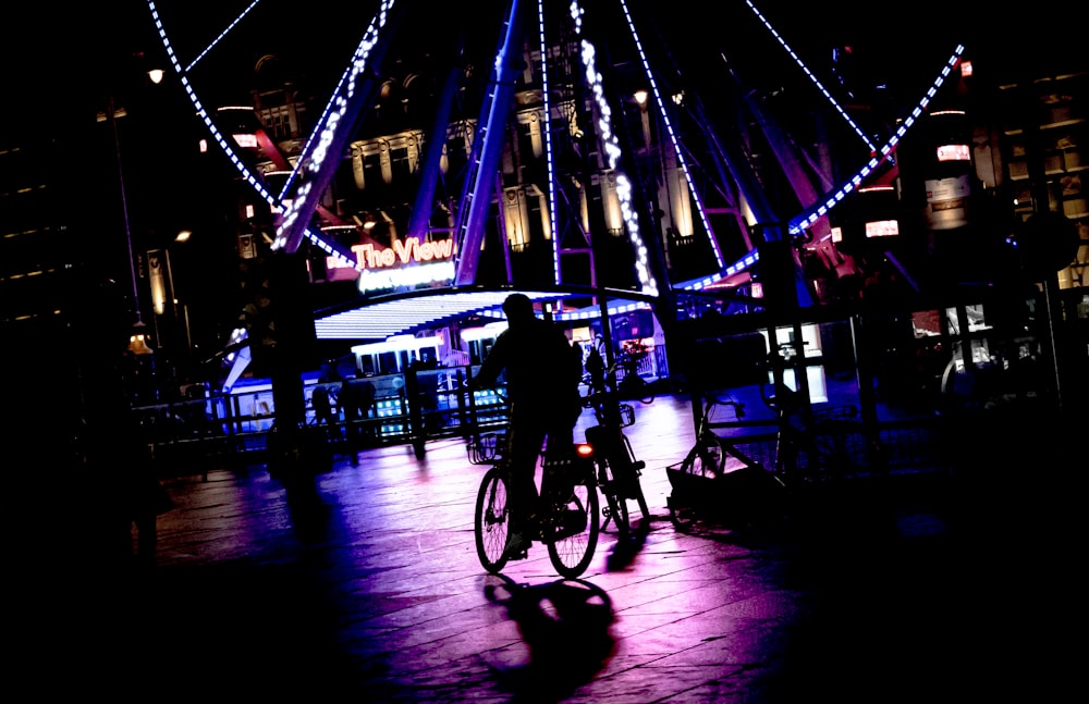 a man riding a bike down a street next to a ferris wheel