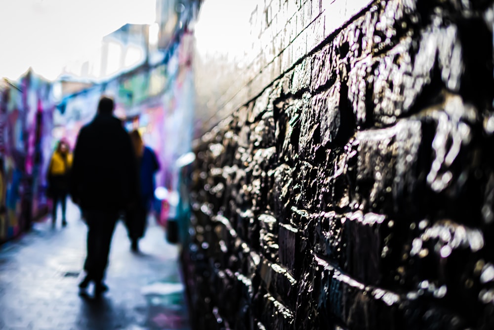 a group of people walking down a street next to a wall