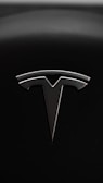 A sleek metallic emblem resembling a stylized letter 'T' is set against a textured black background, suggesting a modern and minimalist design aesthetic.