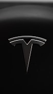 A sleek metallic emblem resembling a stylized letter 'T' is set against a textured black background, suggesting a modern and minimalist design aesthetic.