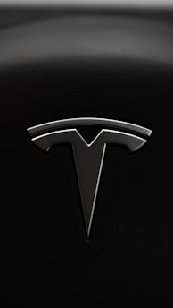A sleek metallic emblem resembling a stylized letter 'T' is set against a textured black background, suggesting a modern and minimalist design aesthetic.