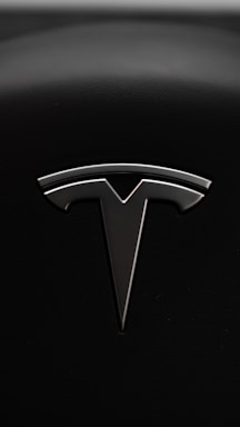 A sleek metallic emblem resembling a stylized letter 'T' is set against a textured black background, suggesting a modern and minimalist design aesthetic.