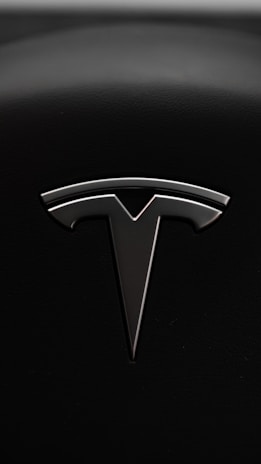 A sleek metallic emblem resembling a stylized letter 'T' is set against a textured black background, suggesting a modern and minimalist design aesthetic.