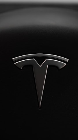 A sleek metallic emblem resembling a stylized letter 'T' is set against a textured black background, suggesting a modern and minimalist design aesthetic.