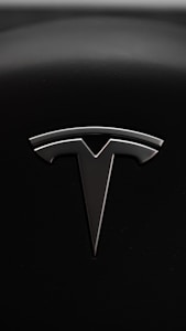 A sleek metallic emblem resembling a stylized letter 'T' is set against a textured black background, suggesting a modern and minimalist design aesthetic.