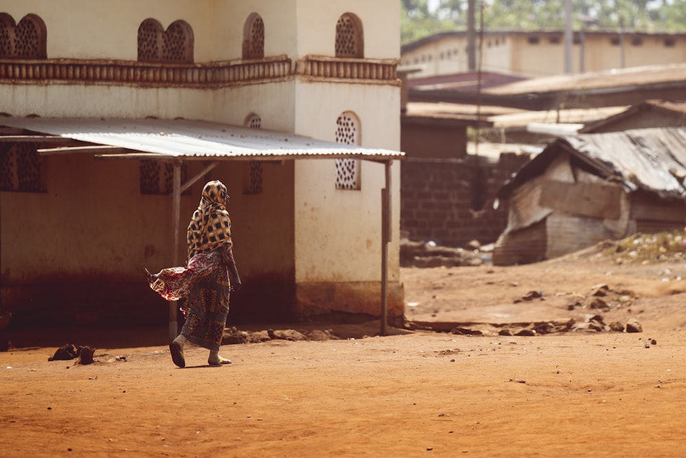 a woman walking down a dirt road next to a building