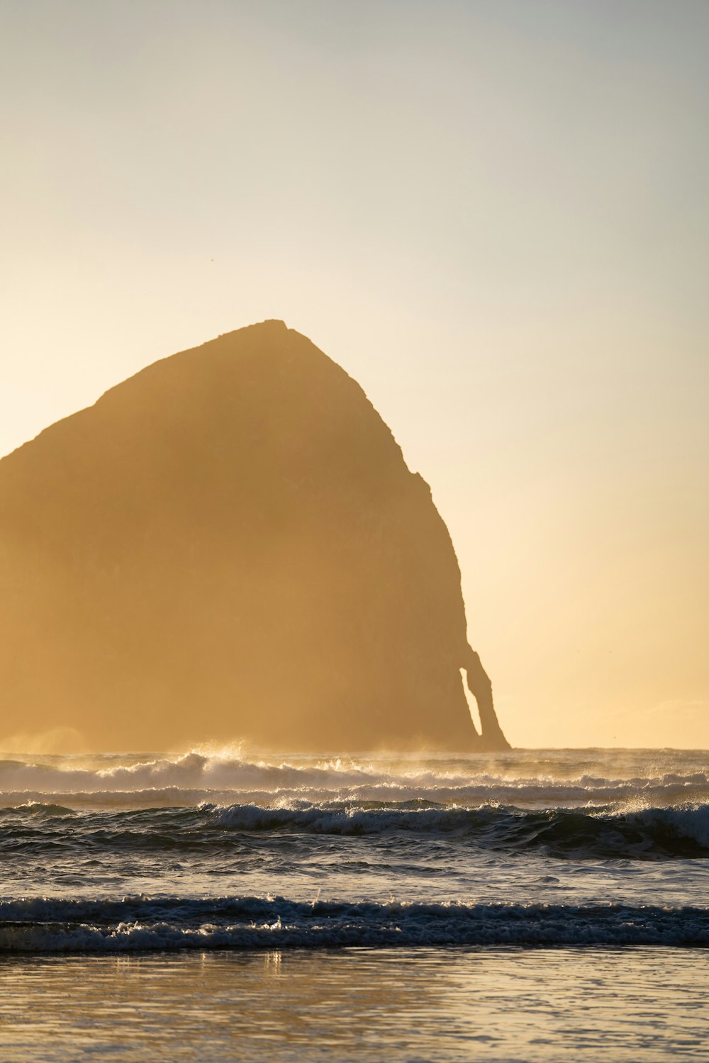 a large rock sitting on top of a beach next to the ocean