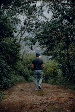 a man walking down a dirt road in the woods