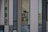 Several large windows reveal a sparse office interior with modern white office chairs and black monitors against a backdrop of a minimalist, multi-textured building facade.