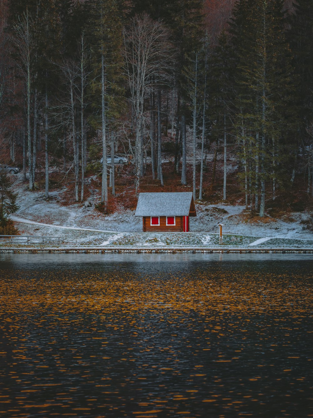 a red house sitting on top of a lake next to a forest