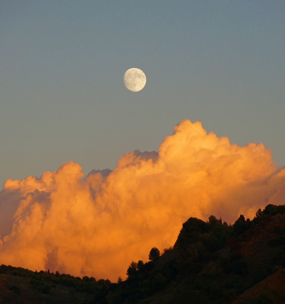 a full moon is seen above the clouds