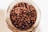 Coffee beans are seen inside a glass jar, with a close-up perspective highlighting their rich, brown tones and glossy textures.
