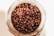Coffee beans are seen inside a glass jar, with a close-up perspective highlighting their rich, brown tones and glossy textures.