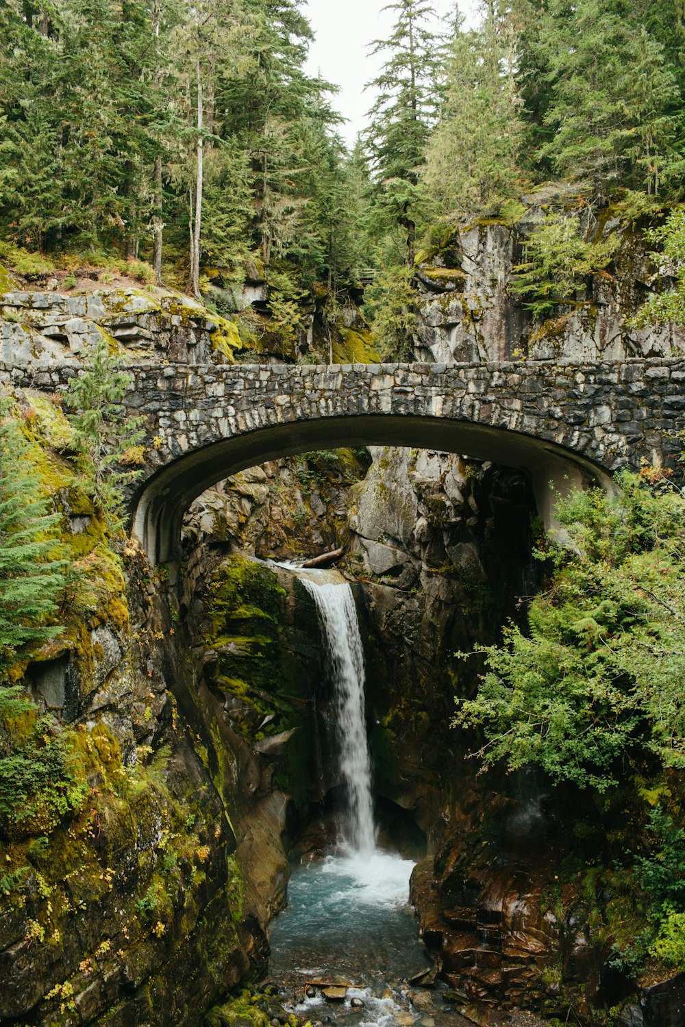 a waterfall under a bridge with a stone bridge over it
