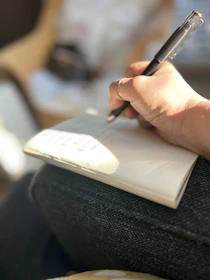 a person writing on a notebook with a pen