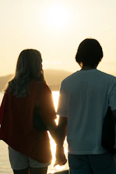 A romantic sunset view over a serene beach with a couple holding hands.