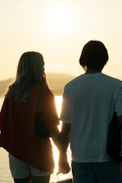 A romantic sunset view over a serene beach with a couple holding hands.