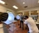 A photographer is taking pictures of a food setup in a studio or kitchen environment. The scene includes professional lighting equipment, such as softboxes and reflectors. Two individuals are present, with one focusing on capturing the image while the other stands nearby.
