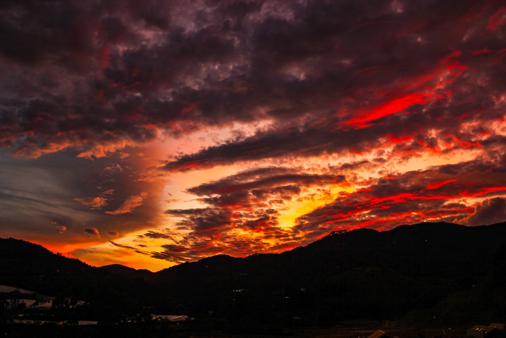a red and yellow sunset with clouds and mountains in the background