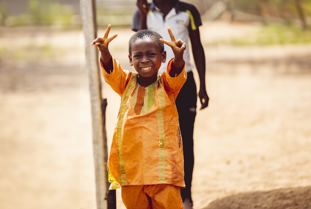 a young boy standing in front of a pole with his hands in the air