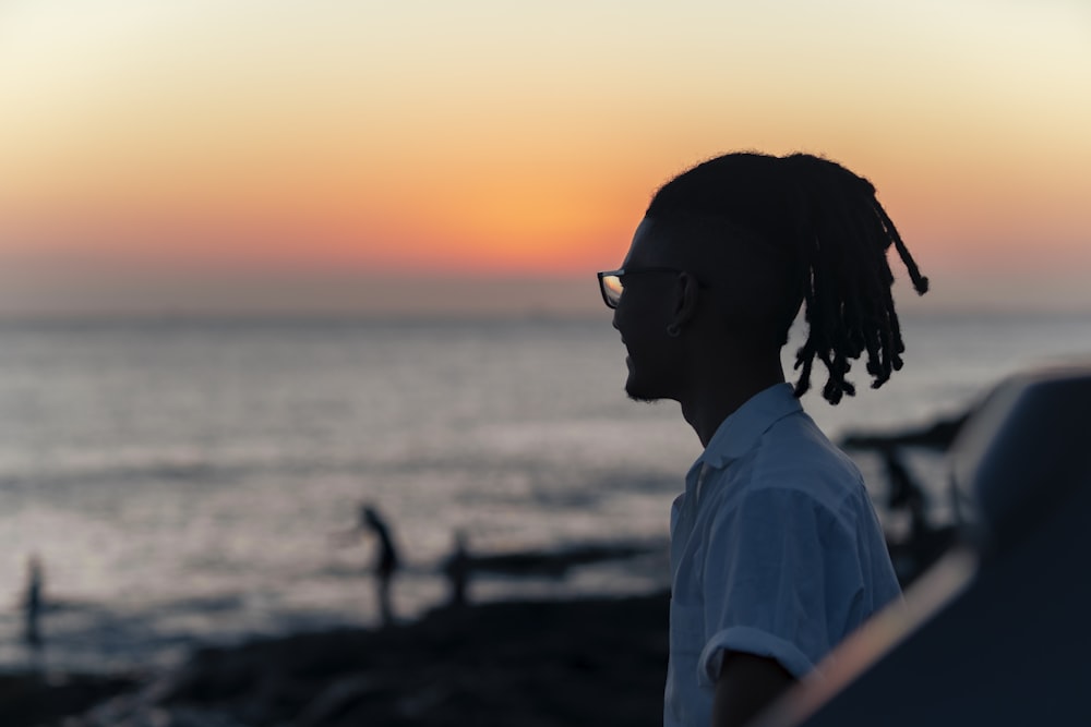 a man with dreadlocks standing in front of the ocean