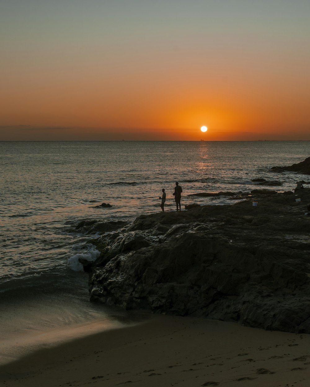 a couple of people standing on top of a sandy beach