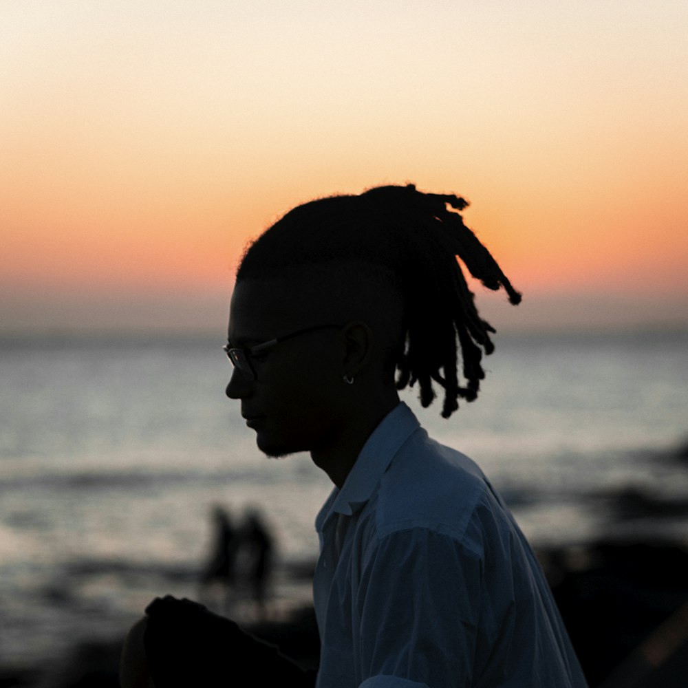 a man with dreadlocks standing in front of the ocean