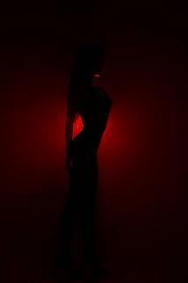 Elegant silhouette of a model against a dark backdrop with red light accents.