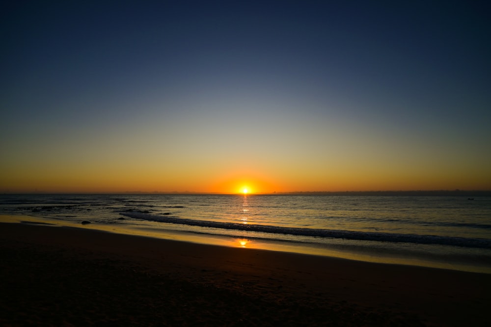 the sun is setting over the ocean on the beach