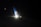A dimly lit airplane wing with a logo is visible against the dark night sky. There is a bright light illuminating a section of the wing.