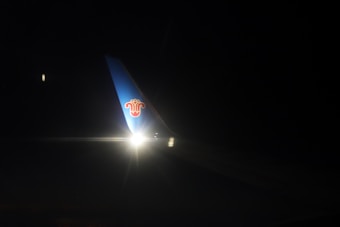 A dimly lit airplane wing with a logo is visible against the dark night sky. There is a bright light illuminating a section of the wing.