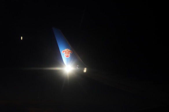 A dimly lit airplane wing with a logo is visible against the dark night sky. There is a bright light illuminating a section of the wing.