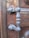 An ornate metallic door handle with intricate designs, mounted on a wooden door. The wood shows signs of age and natural texture, complementing the vintage appearance of the handle.