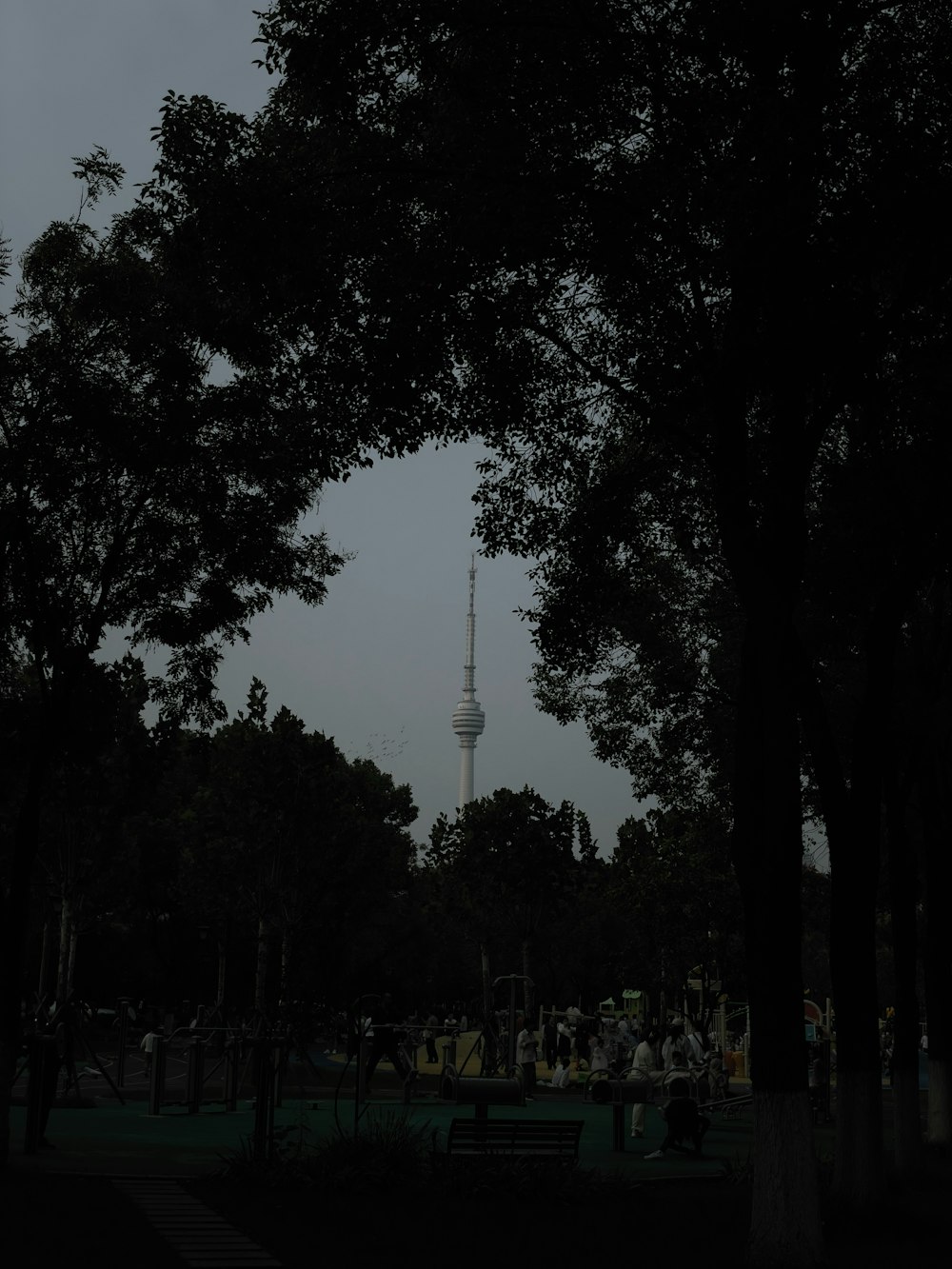 a dark picture of a park with a tower in the background