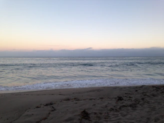 A serene beach at sunrise with gentle waves lapping the shore.