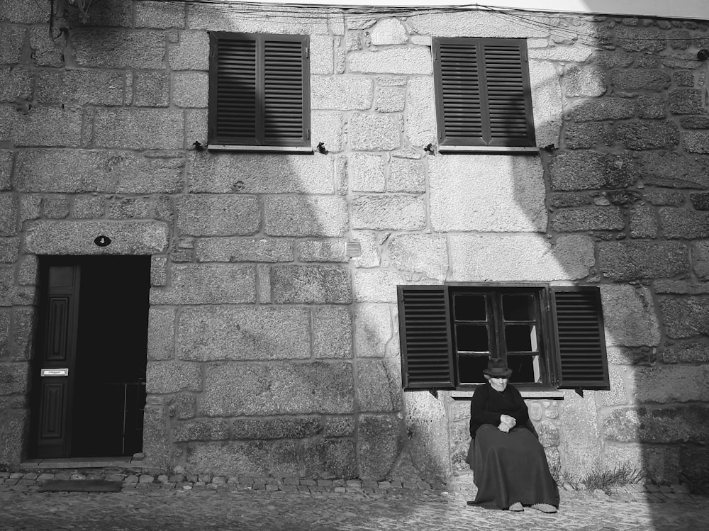 a black and white photo of a woman sitting in front of a building