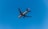 A commercial airplane flies against a clear blue sky, with the word 'Qatar' visible on the side of the aircraft. The airplane is captured from below, revealing the underside of its wings and fuselage.