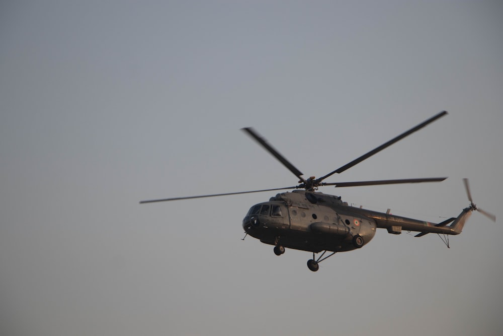 a military helicopter flying through a gray sky