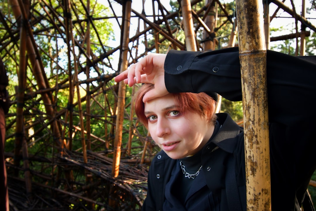 a woman with red hair leaning against a wooden pole, A person looking confusingly at the camera in a climbing sculpture