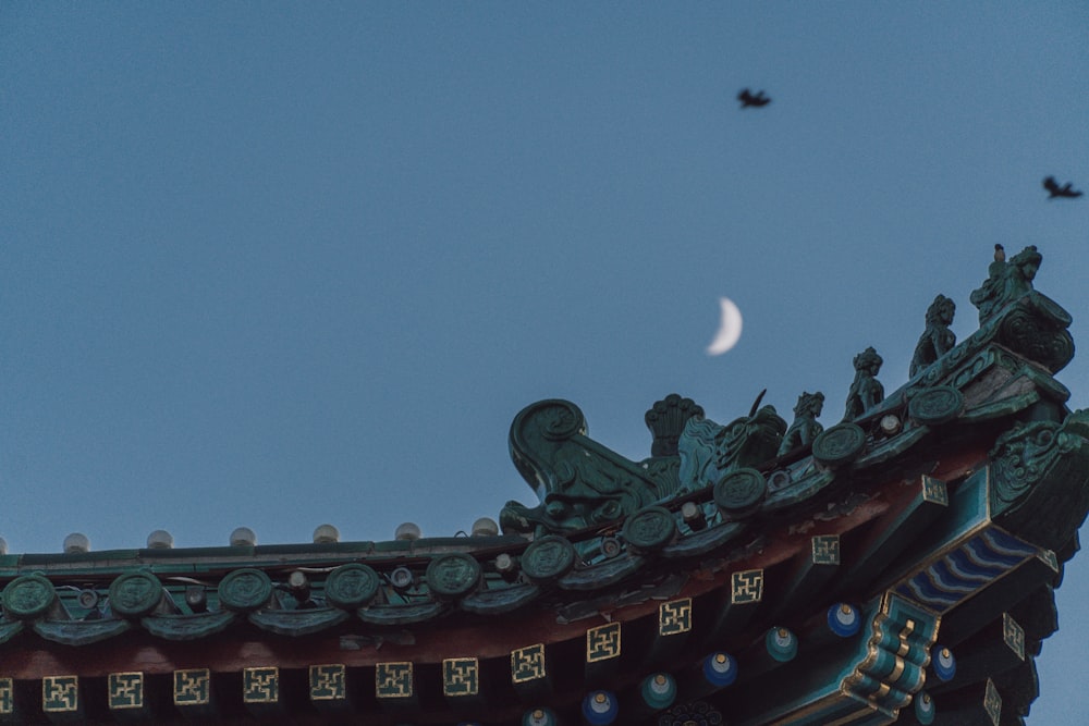 a bird flying over a building with a half moon in the sky