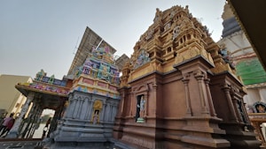 An intricately carved temple structure featuring vibrant statues and ornate designs, with solar panels visible in the background. The temple showcases a combination of colorful deities and traditional architectural elements.