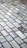 A detailed pattern of rectangular marble tiles with varying shades of gray and white, bordered by thin dark brown grout lines. The tiles are laid out in an offset arrangement, creating a visually interesting grid.