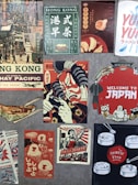 A collage of vintage and retro-style posters featuring various Asian themes. The top left depicts a bustling Hong Kong street scene, while nearby posters advertise drinks and dumplings in vibrant colors. Another central poster displays a samurai in red and blue hues. The bottom right features dim sum illustrations with the label 'Chinese Food'. Elements of Japanese culture, such as a welcome sign with traditional icons, are also present.
