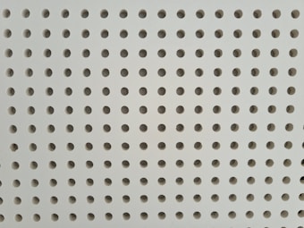 A perforated surface featuring a grid of uniformly spaced circular holes. The background is a light gray or beige material.