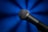 A close-up view of a handheld microphone with a textured metal grille and a dark matte finish, set against a vibrant blue background that radiates soft light effects.