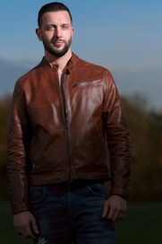 a man wearing a brown leather jacket standing in a field