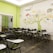 An empty classroom with rows of black chairs featuring attached writing surfaces. The room has a vibrant mural on the wall, depicting a tree with colorful elements and words related to business and creativity. The overall setting is bright with a combination of lime green and white colors on the walls.